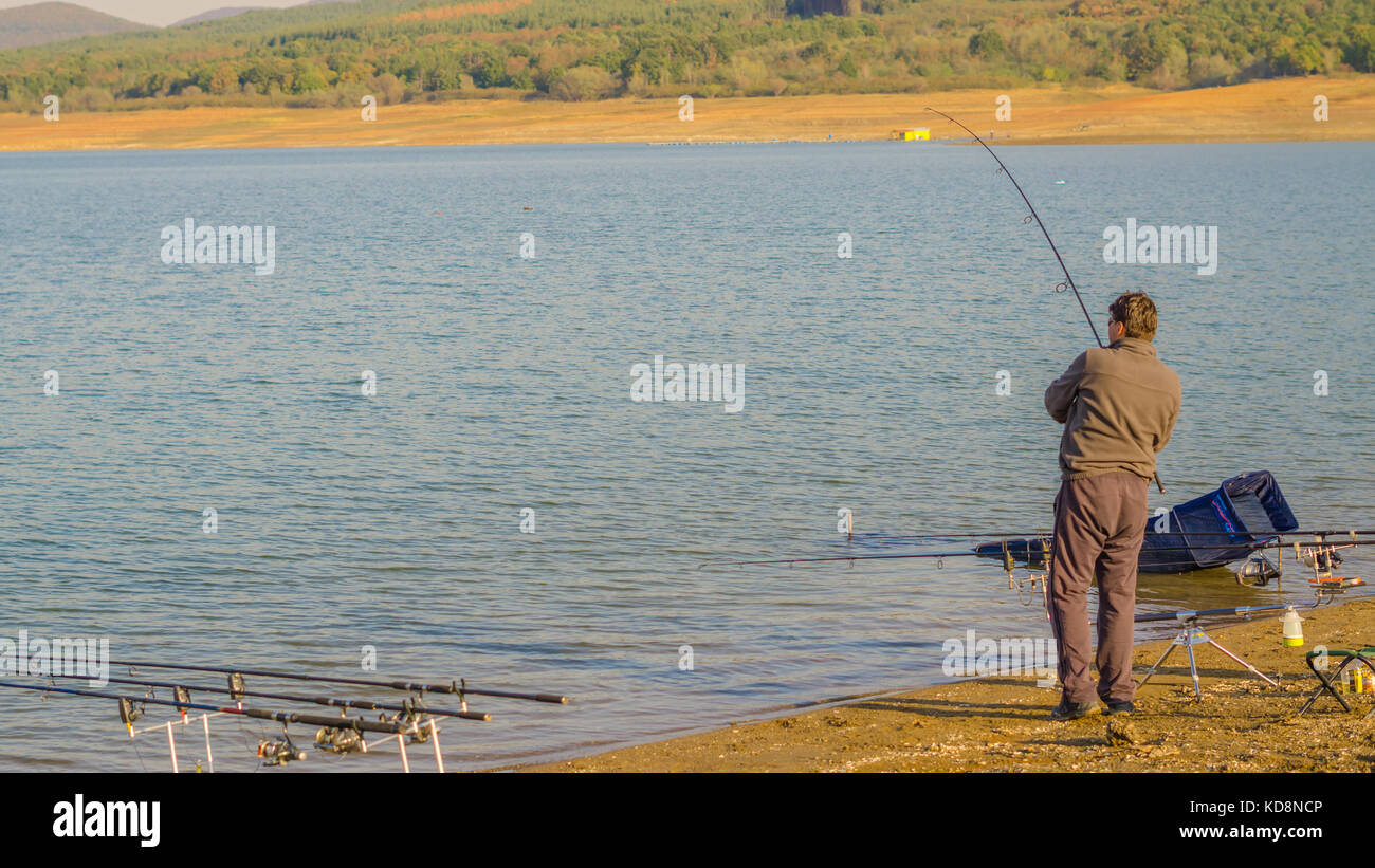 Jrebchevo Dam, Bulgaria a man caught fish on the fishing line trying to get  it out on the shore. Stock Photo
