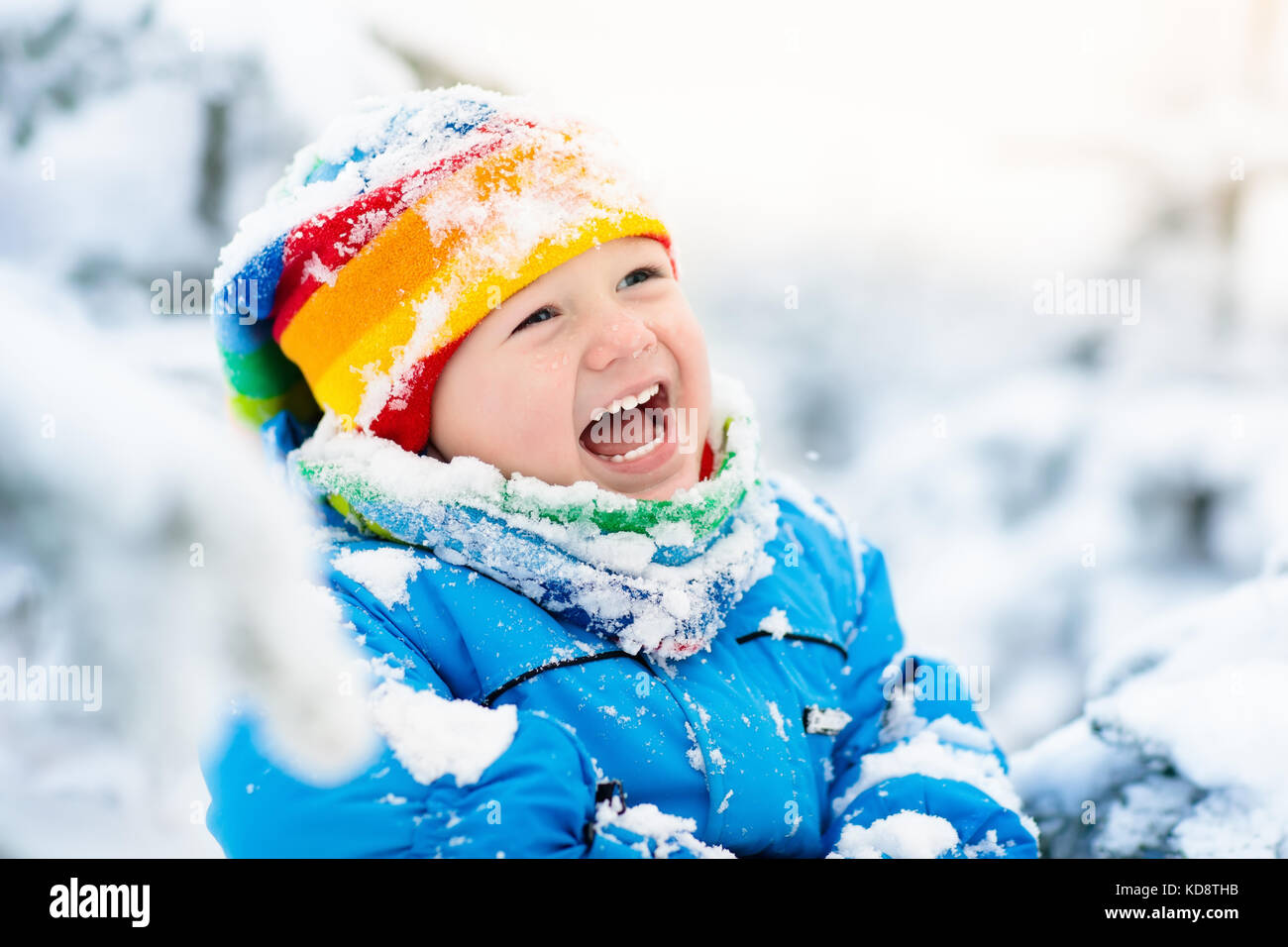 Baby playing with snow in winter. Little toddler boy in blue jacket and ...