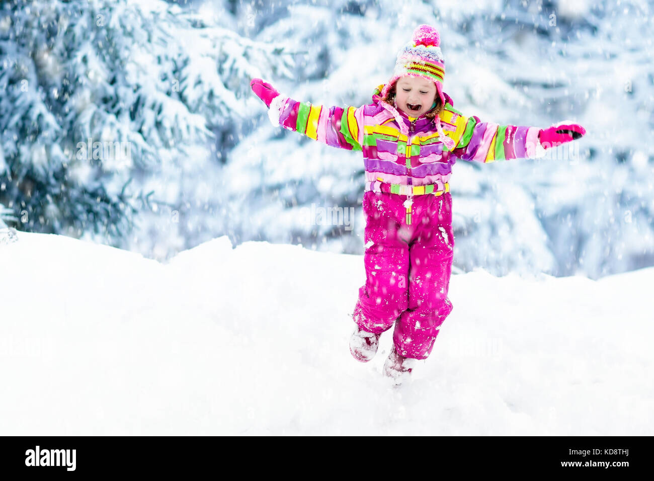 Child playing with snow in winter. Little girl in colorful jacket and ...