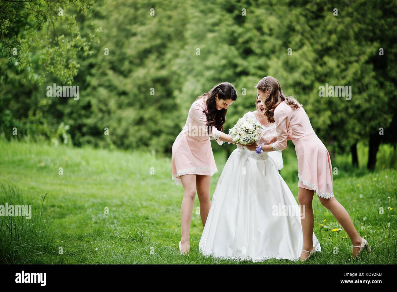 Attractive bride posing and having fun with two her bridesmaids in the park on a sunny spring wedding day. Stock Photo