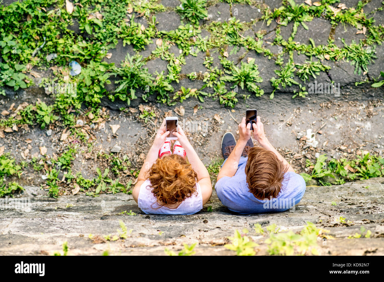 Young couple with smart phones in town, reading or watching something. Sunny spring day. High angle view. Stock Photo