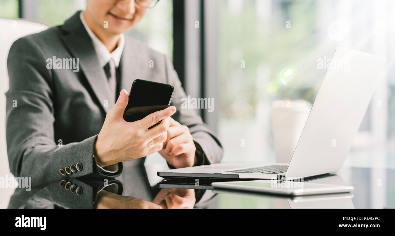 Young businessman or entrepreneur using smartphone, laptop, and digital tablet at work in modern office. Business communication or technology concept Stock Photo