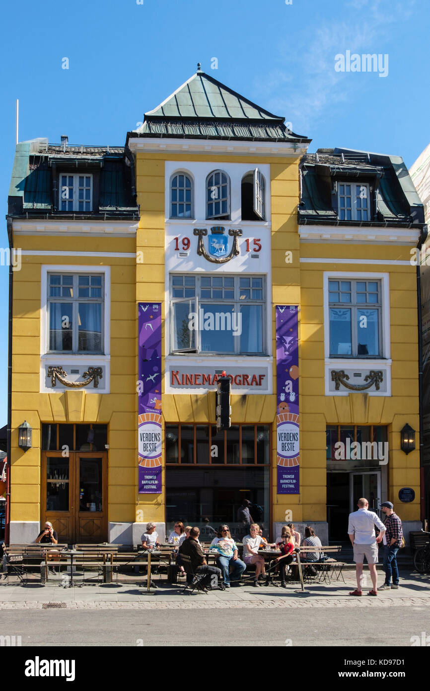 Old Kinematograf cinema in traditional yellow Norwegian building 1915 with people in street cafe. Storgata, Tromso, Troms county, Norway, Scandinavia, Stock Photo