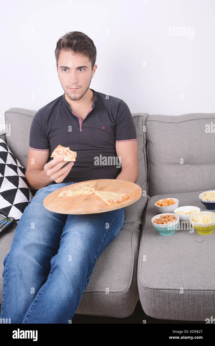 Attractive young man eating pizza on couch. Indoors. Stock Photo