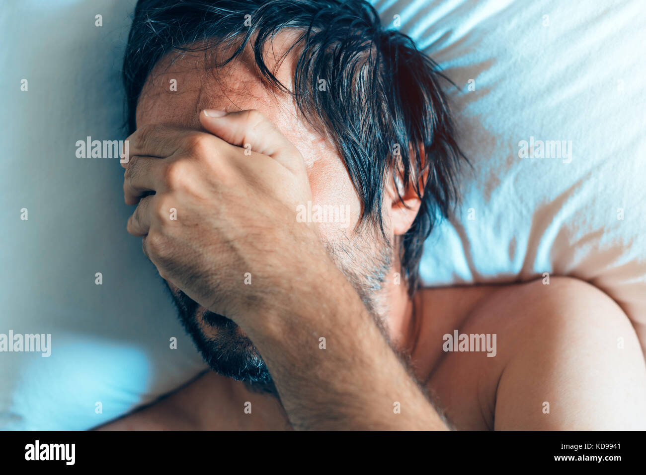Morning depression and midlife crisis of a man in his 40s lying in bed in morning with symptoms like extreme sadness, frustration, anger and fatigue. Stock Photo