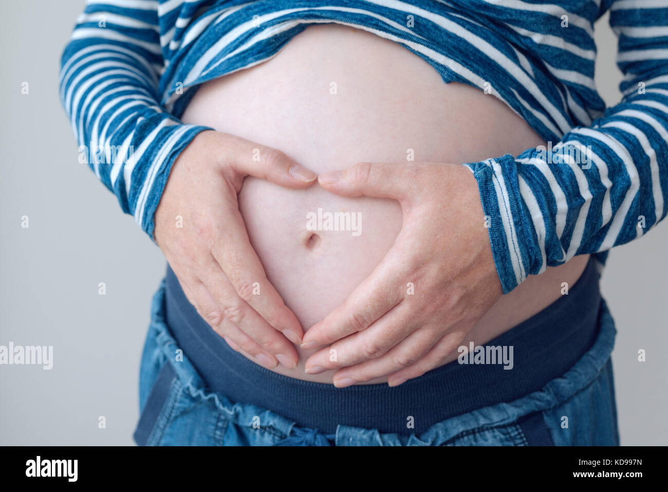 Pregnant woman touching and rubbing her belly, mother stroking and stimulating abdomen, adult caucasian female in fifth month or twenty first week of  Stock Photo