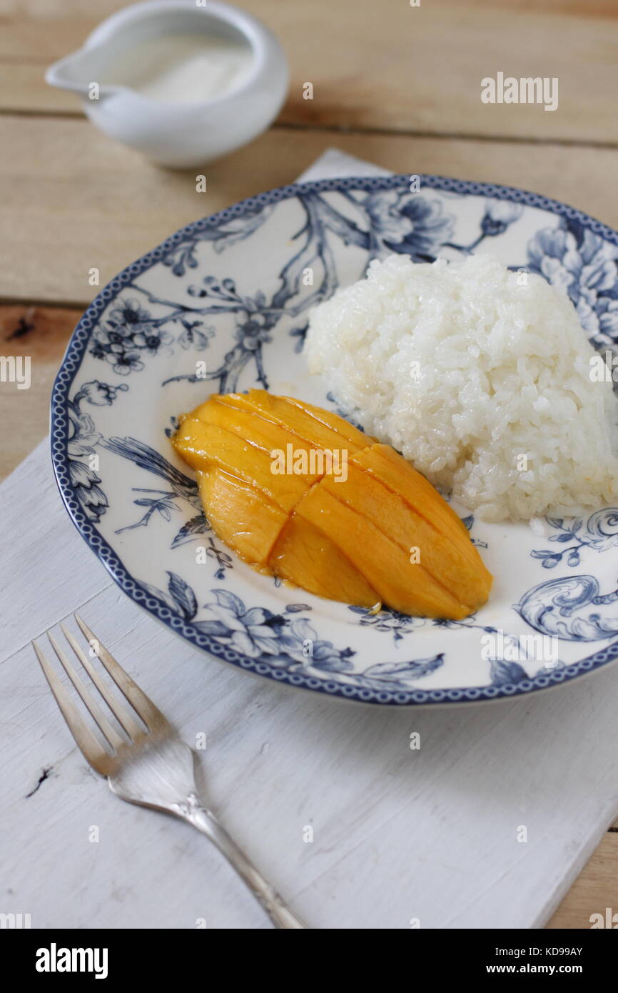 Sweet thai sticky rice with slices of mango on blue plate over whitish board Stock Photo