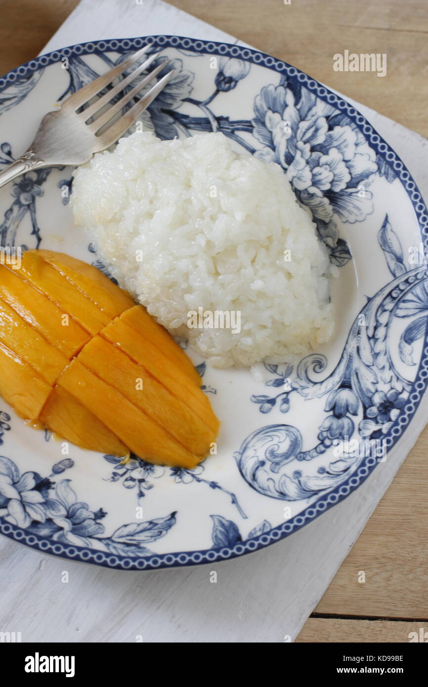 Sweet thai sticky rice with slices of mango on blue plate over whitish