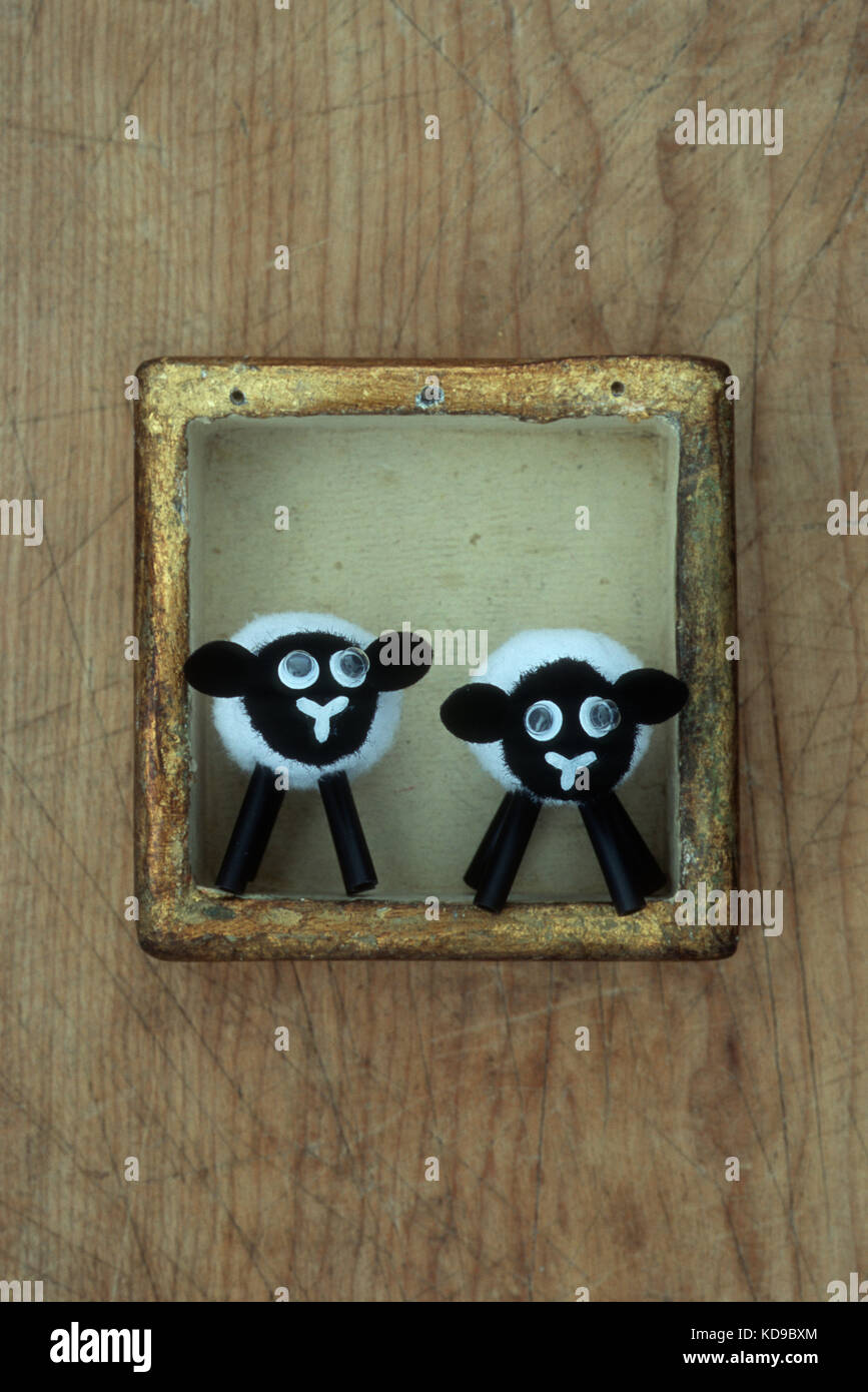 Two comical small models of black and white sheep with bulbous eyes standing in small gold box Stock Photo