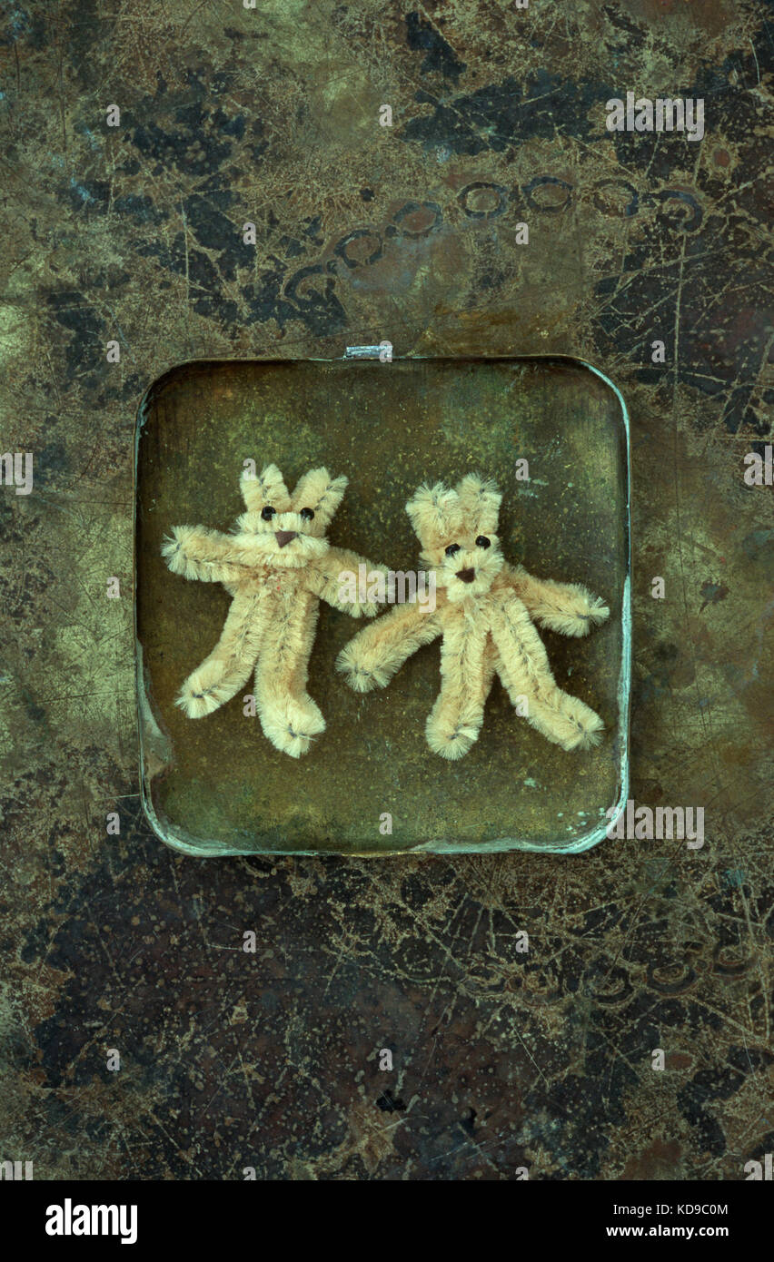 Two small beige teddy bears made from pipe cleaners lying in brass box on tarnished brass Stock Photo