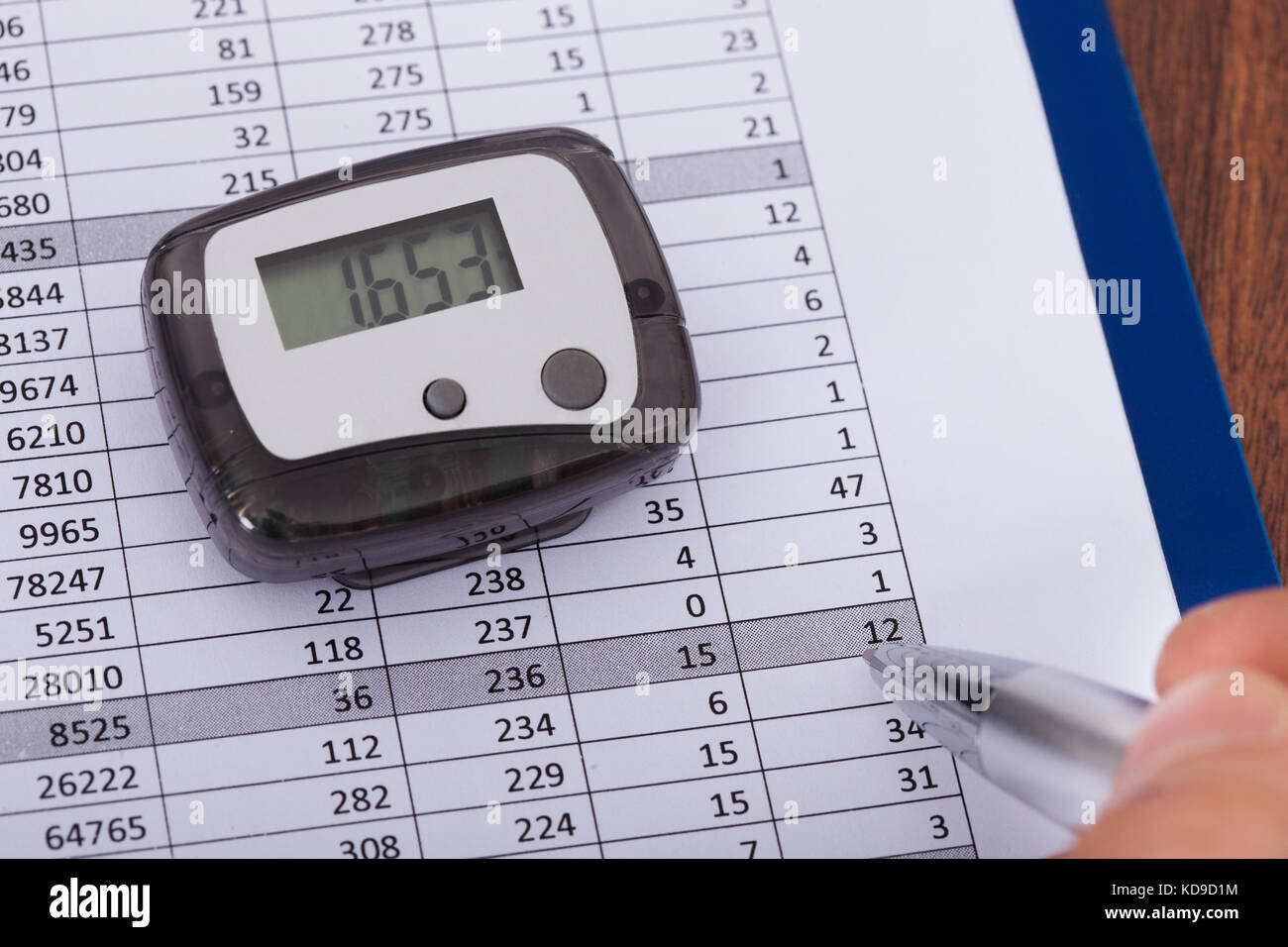 Close-up Of Hand Holding Pen Over Sheet With Digital Pedometer Stock Photo