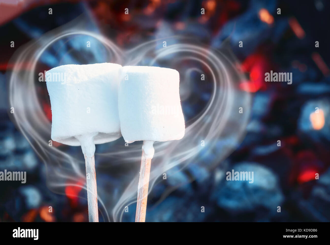 Two white sweet marshmallows roasting over fire flames. Smoke in form