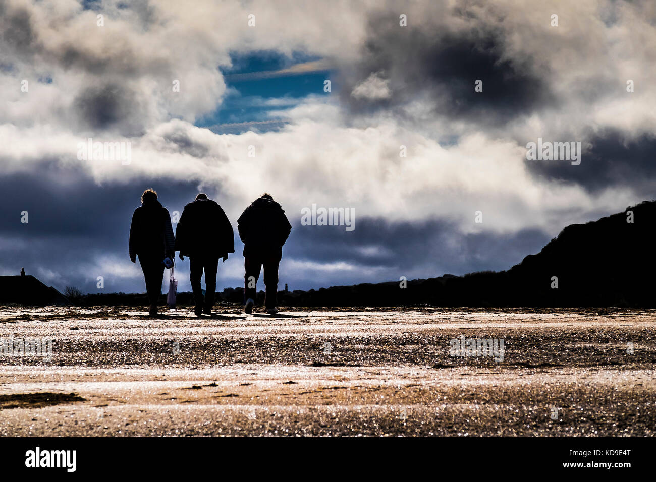 People seen in silhouette - three people seen in silhouette as they walk over the beach at Holywell Bay Cornwall. Stock Photo