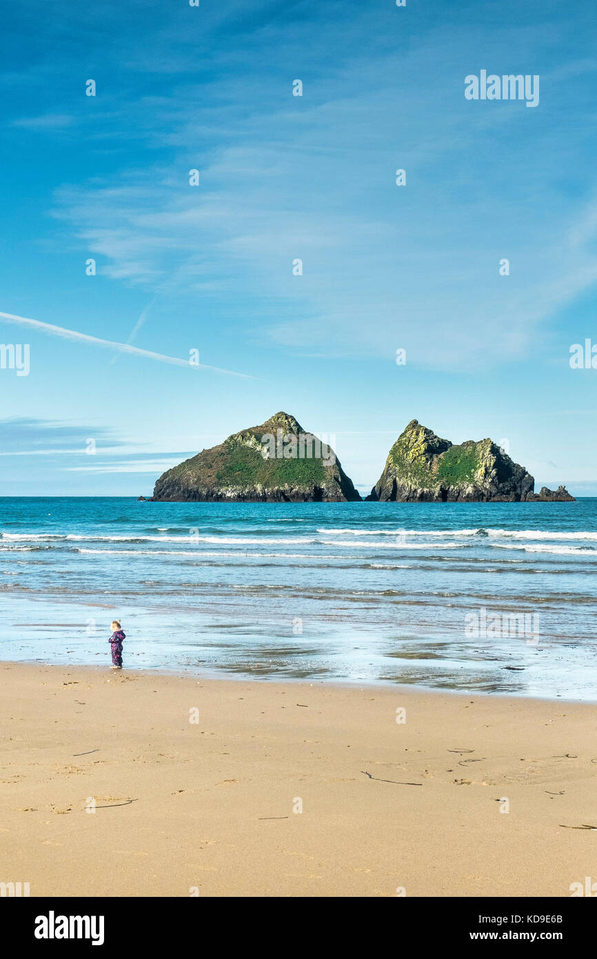 A toddler standing on the beach at Holywell Bay Cornwall. Gull Rocks at