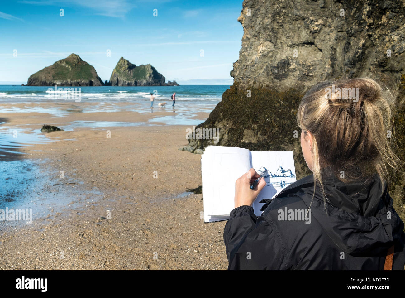 An artist working at Holywell Bay  - an artist drawing a sketch of the iconic Gull Rocks at Holywell Bay in Cornwall one of the Poldark film locations Stock Photo