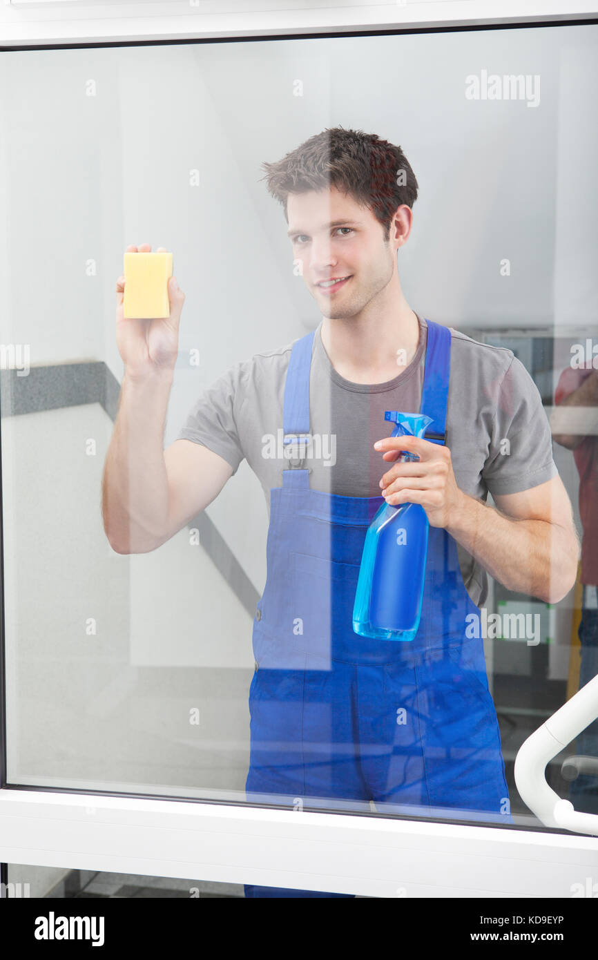 Young Male Cleaner Cleaning The Door Glass With Sponge And Spray Bottle Stock Photo