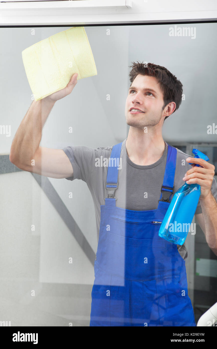 Happy Male Cleaner Cleaning The Glass With Paper And Spray Bottle Stock Photo