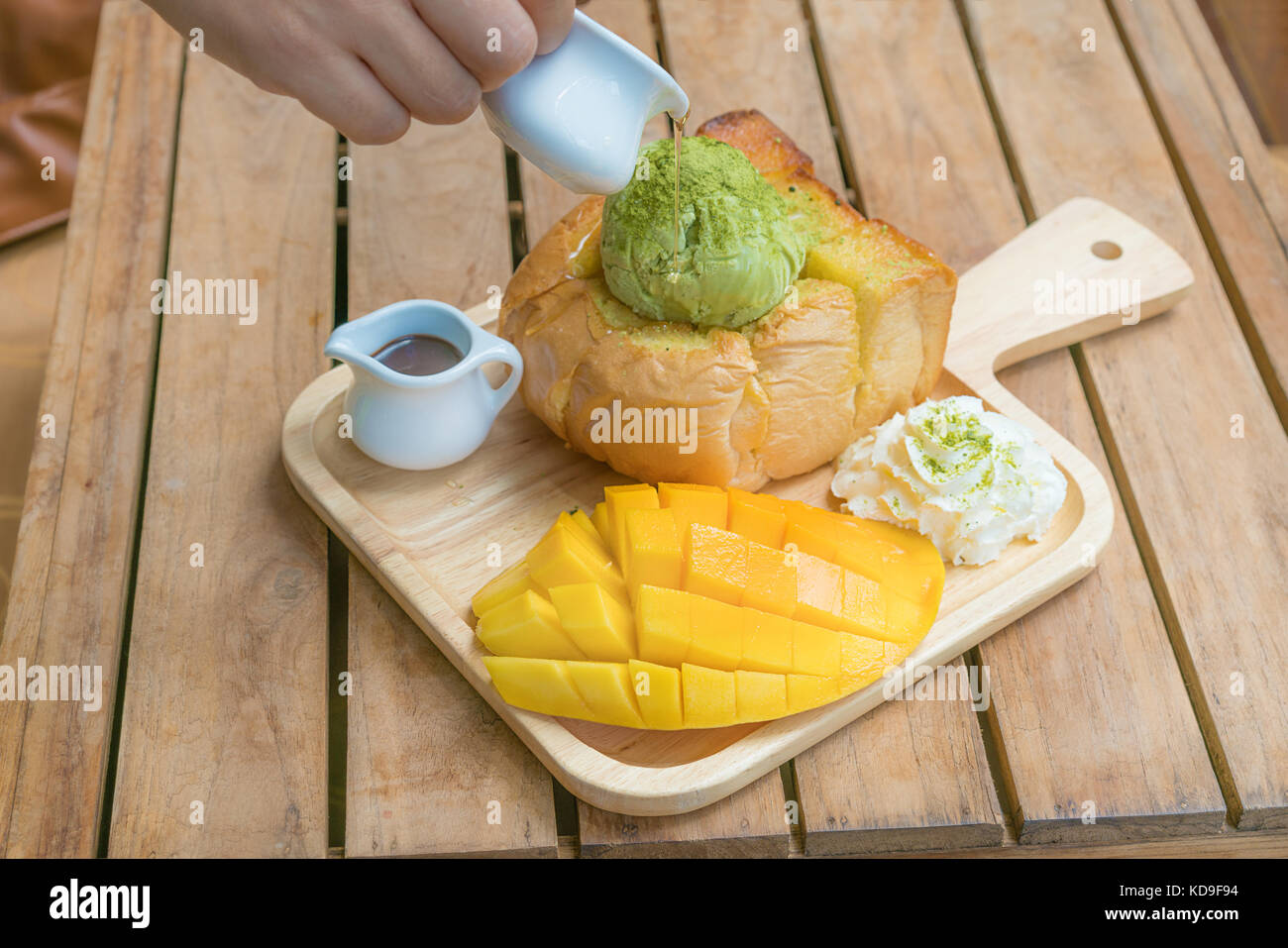 Honey toast green tea ice-cream with ripe barracuda mango and whipping cream in wooden plate on wooden table. Stock Photo