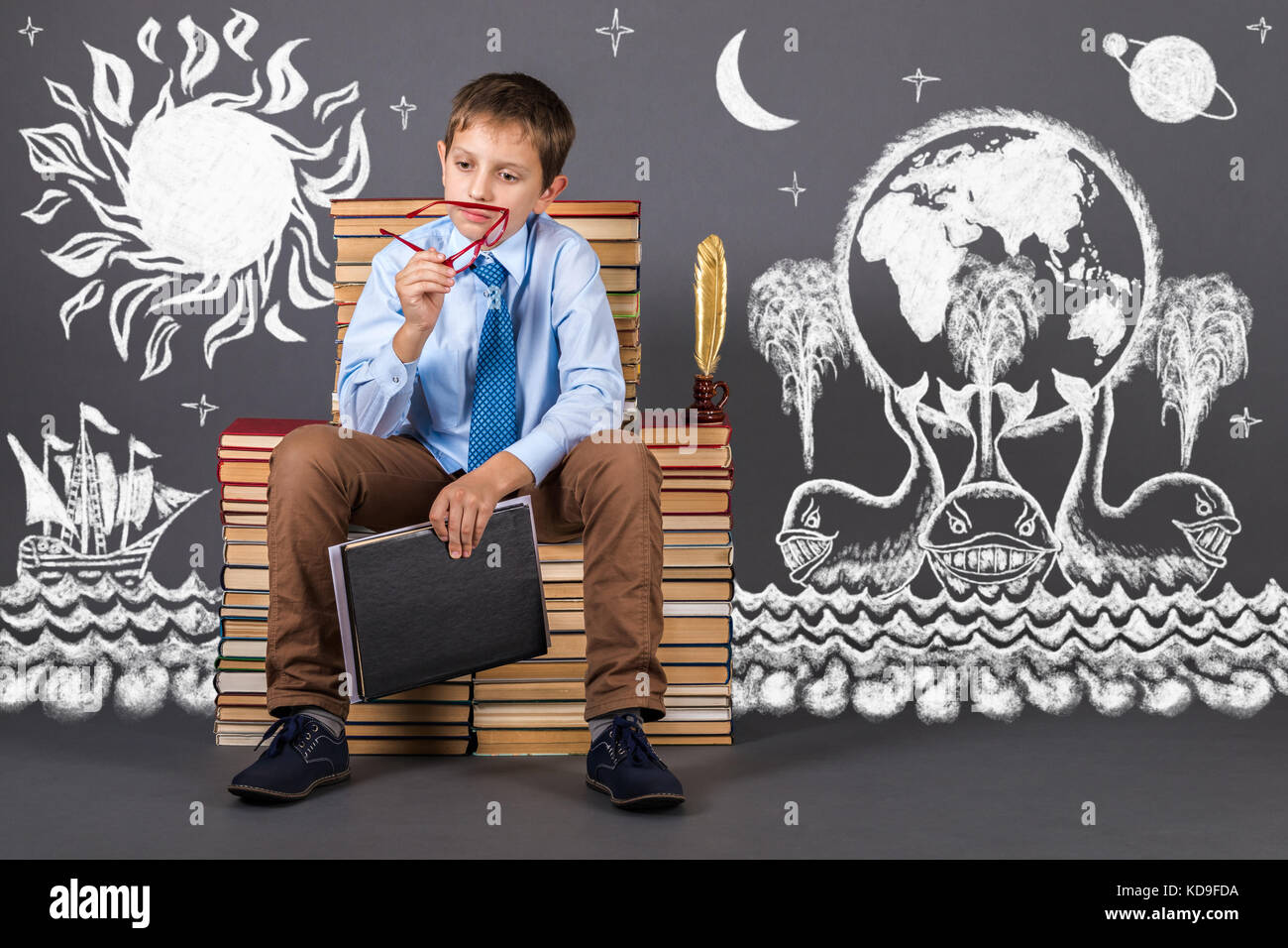 Education idea. A boy sitting on a throne of books, thinking about the structure of the universe Stock Photo