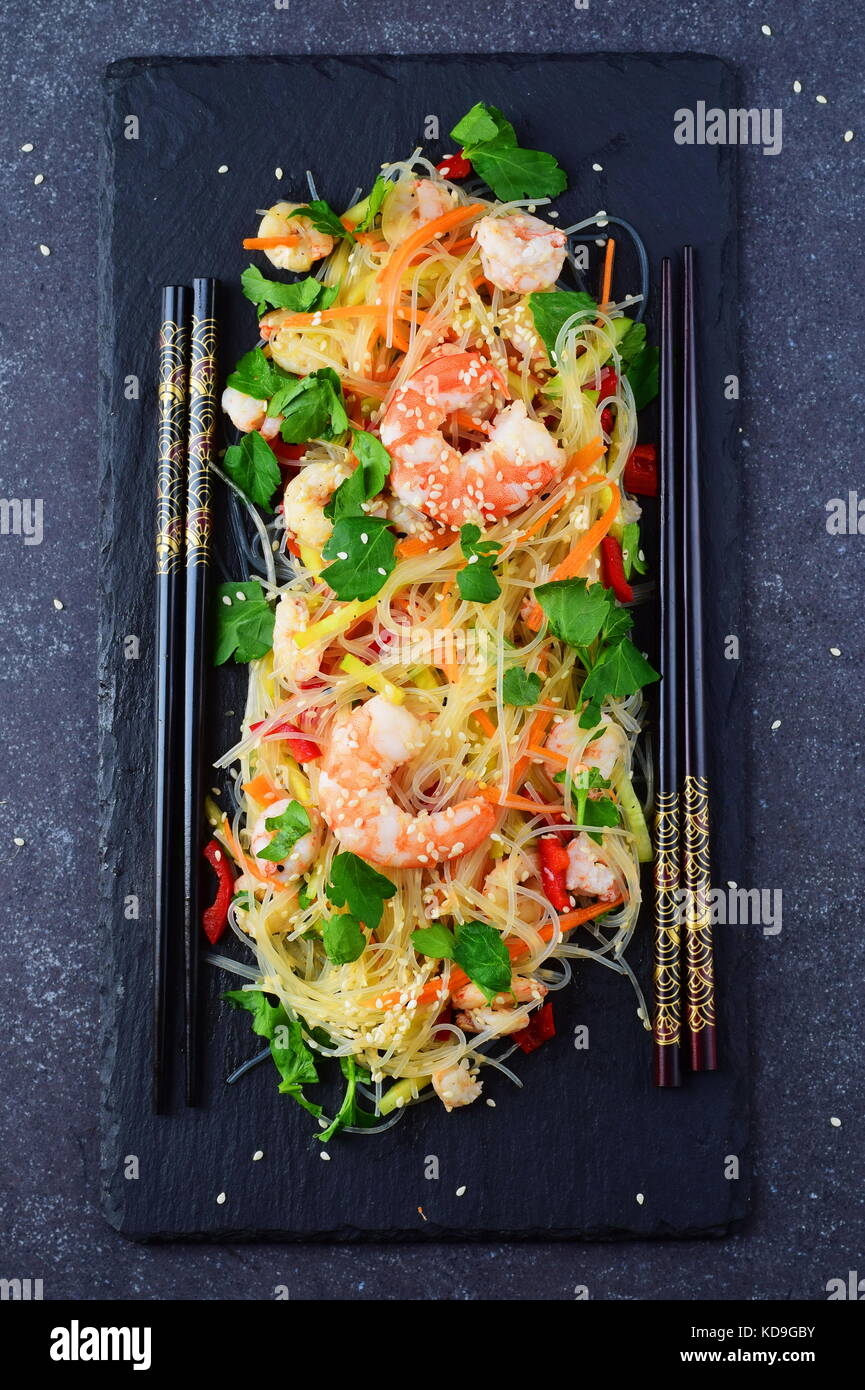 Noodles with prawns and vegetables on a black stone plate on a grey abstract background. Healthy food concept Stock Photo