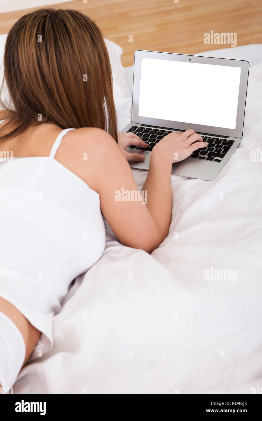 Young Woman Lying On Bed And Using Laptop Stock Photo