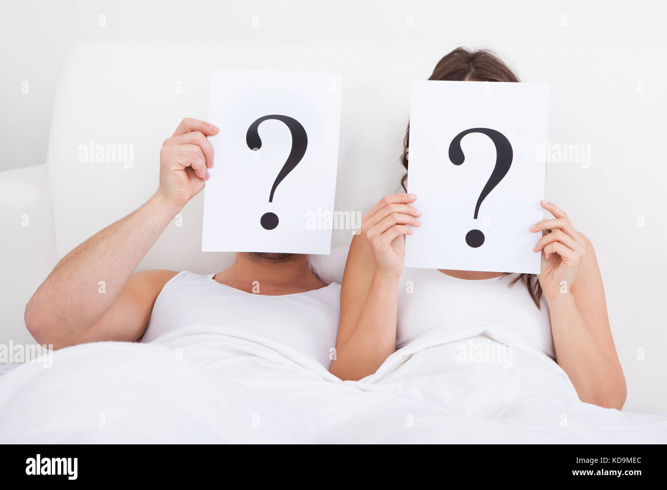 Couple Lying On Bed Holding Question Mark On Face Stock Photo