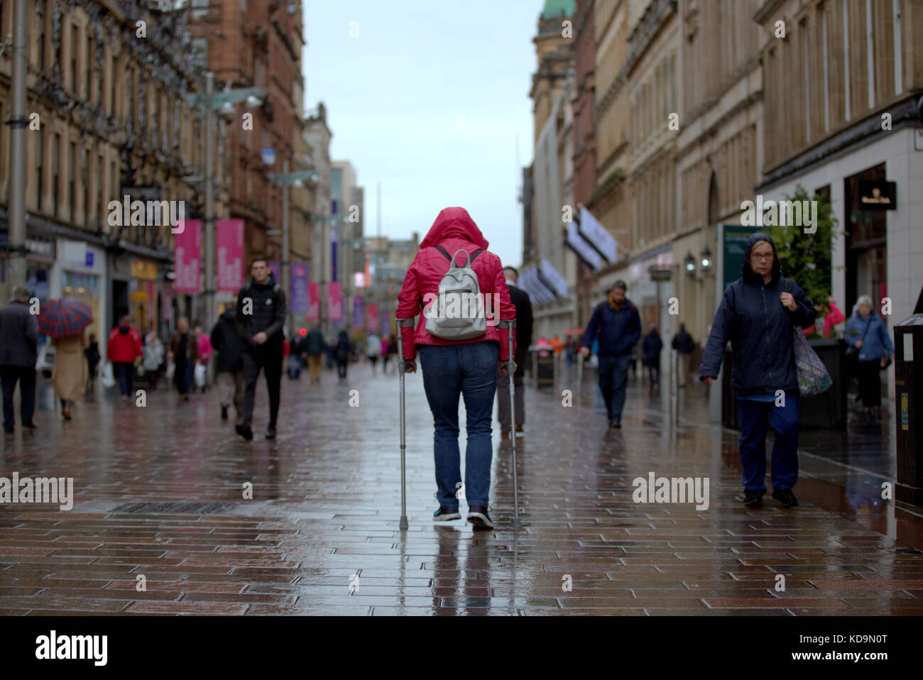 girl with walking sticks on Buchanan street Glasgow in perspective from behind crutches walking aids Stock Photo