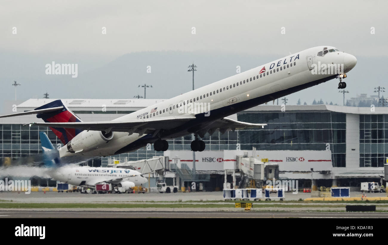 Richmond, British Columbia, Canada. 6th Oct, 2017. A Delta Air Lines McDonnell Douglas MD-90 (N923DN) narrow-body single-aisle regional jet airliner takes off from Vancouver International Airport. In the background: a Westjet Airlines Boeing 737 docked at one of the airport's arrival/departure gates. Credit: Bayne Stanley/ZUMA Wire/Alamy Live News Stock Photo
