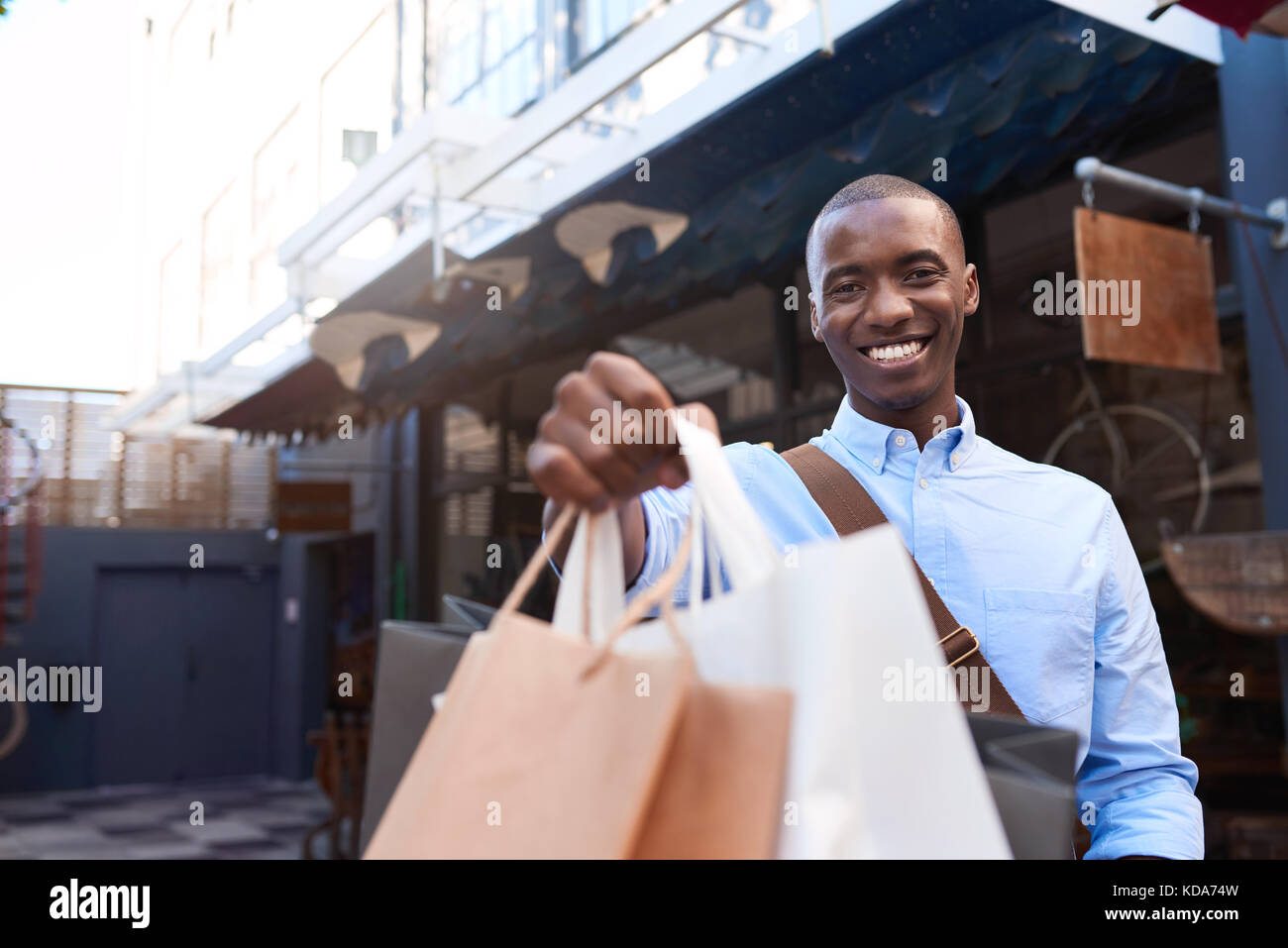 Smiling young man standing outside holding up shopping bags Stock Photo