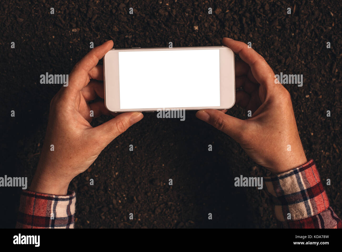 Farmer holding mobile phone over soil ground. Smart phone has blank touch screen as copy space. Stock Photo