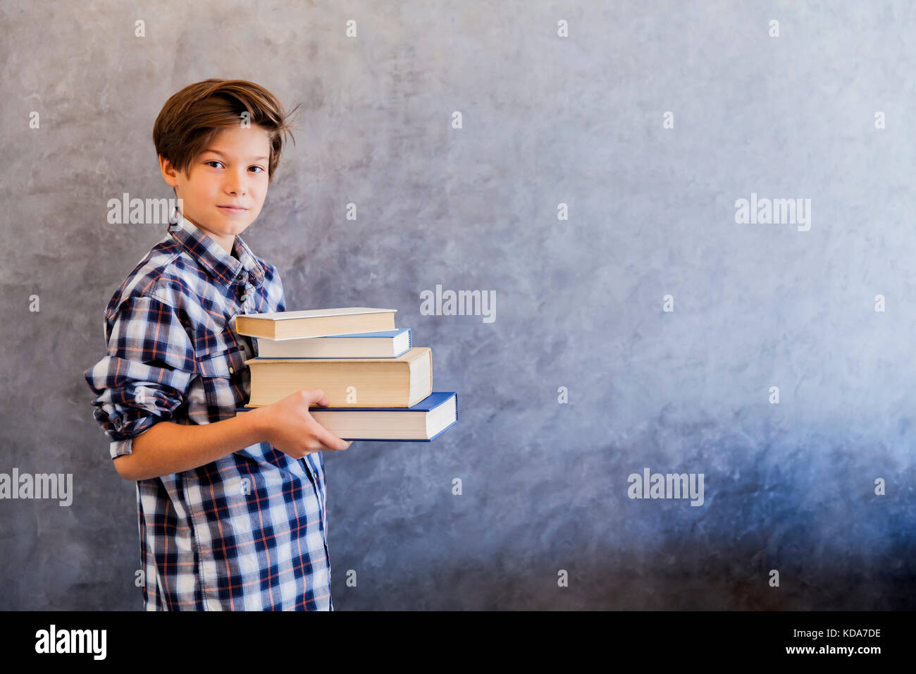 Cute teenage school boy holding books against wall Stock Photo - Alamy