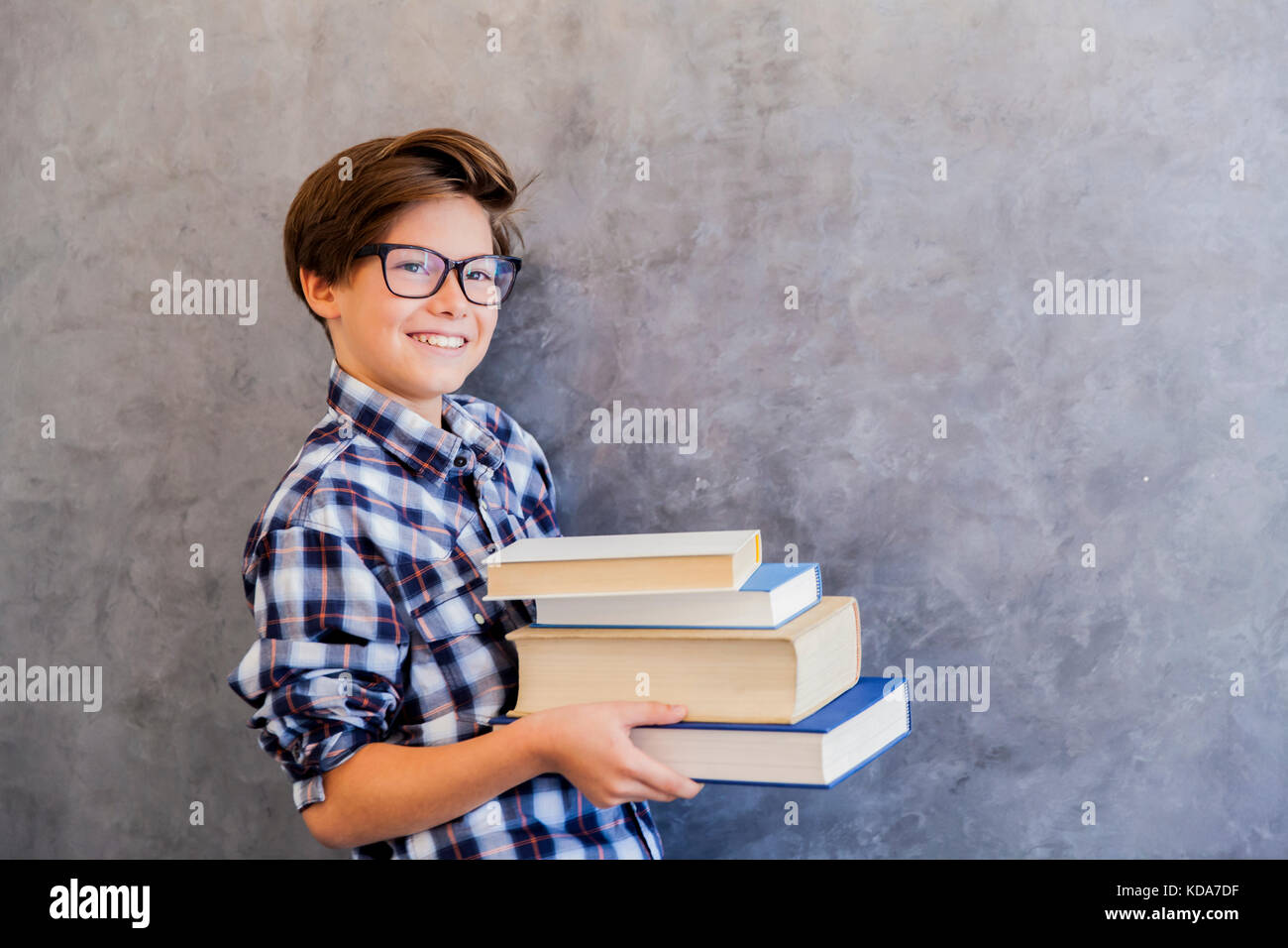 Cute teenage school boy holding books against wall Stock Photo - Alamy