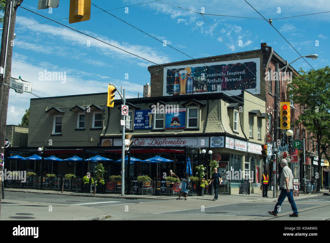 Beer advert sign and Restaurant in Kensington Place Toronto Canada man crossing the road wires cables electricity umbrellas signs sign plants plant Stock Photo