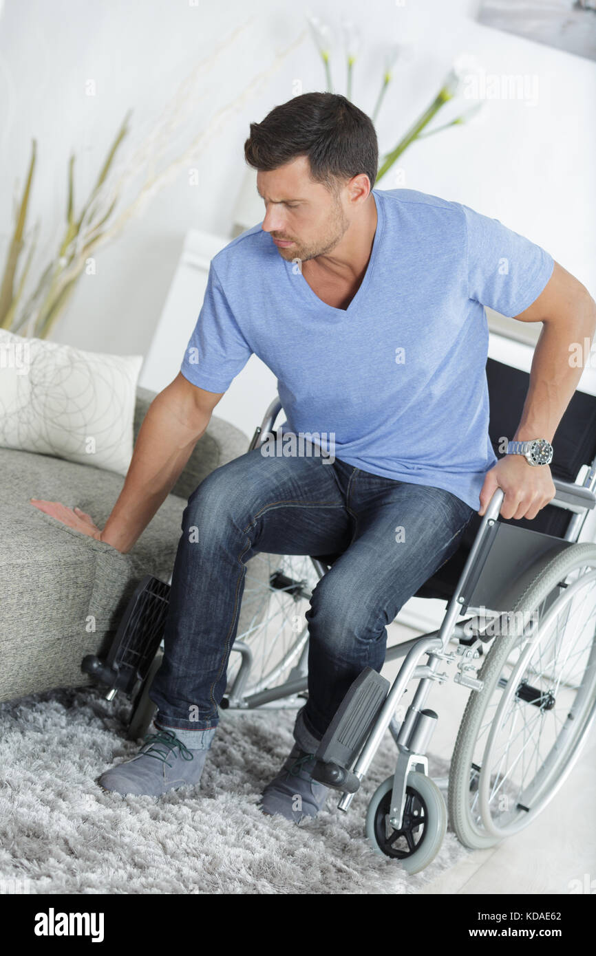 young handsome handicapped man going from wheelchair to sofa Stock