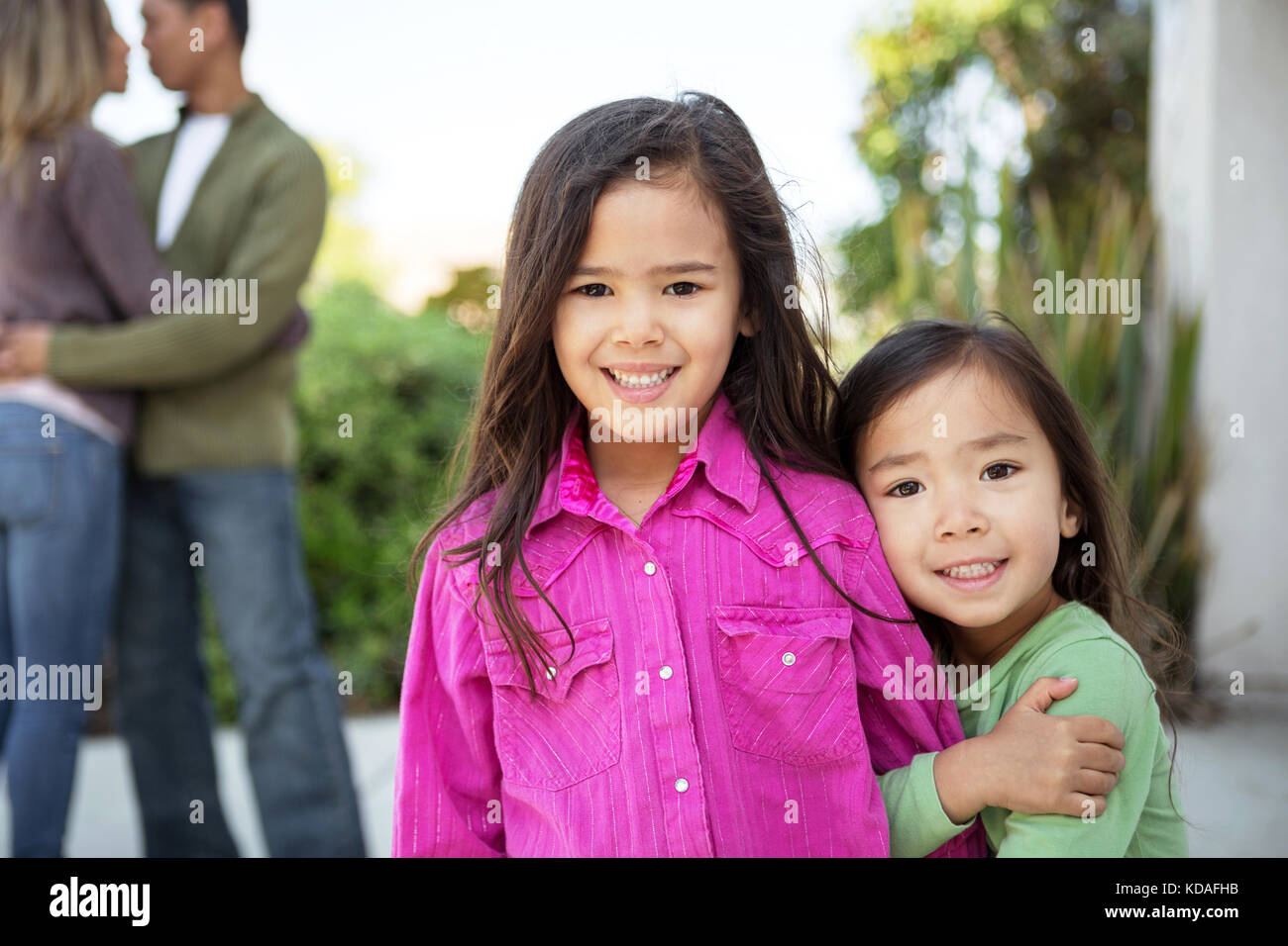 Happy little girls with their parents in the background. Stock Photo