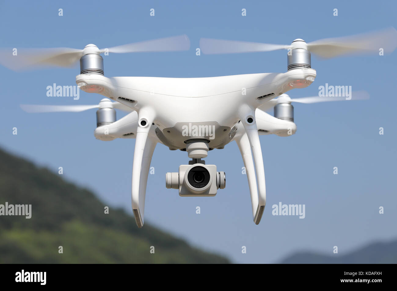 White remote controlled drone flying in clear blue sky with mountain