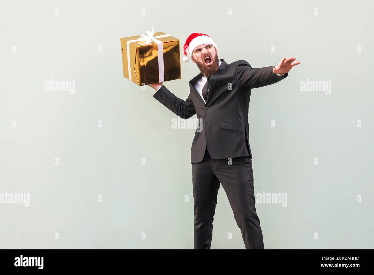 Catch your gift! Young adult well dressed bearded man swung and wants to throw off your gift box, isolated on gray background. Studio shot Stock Photo