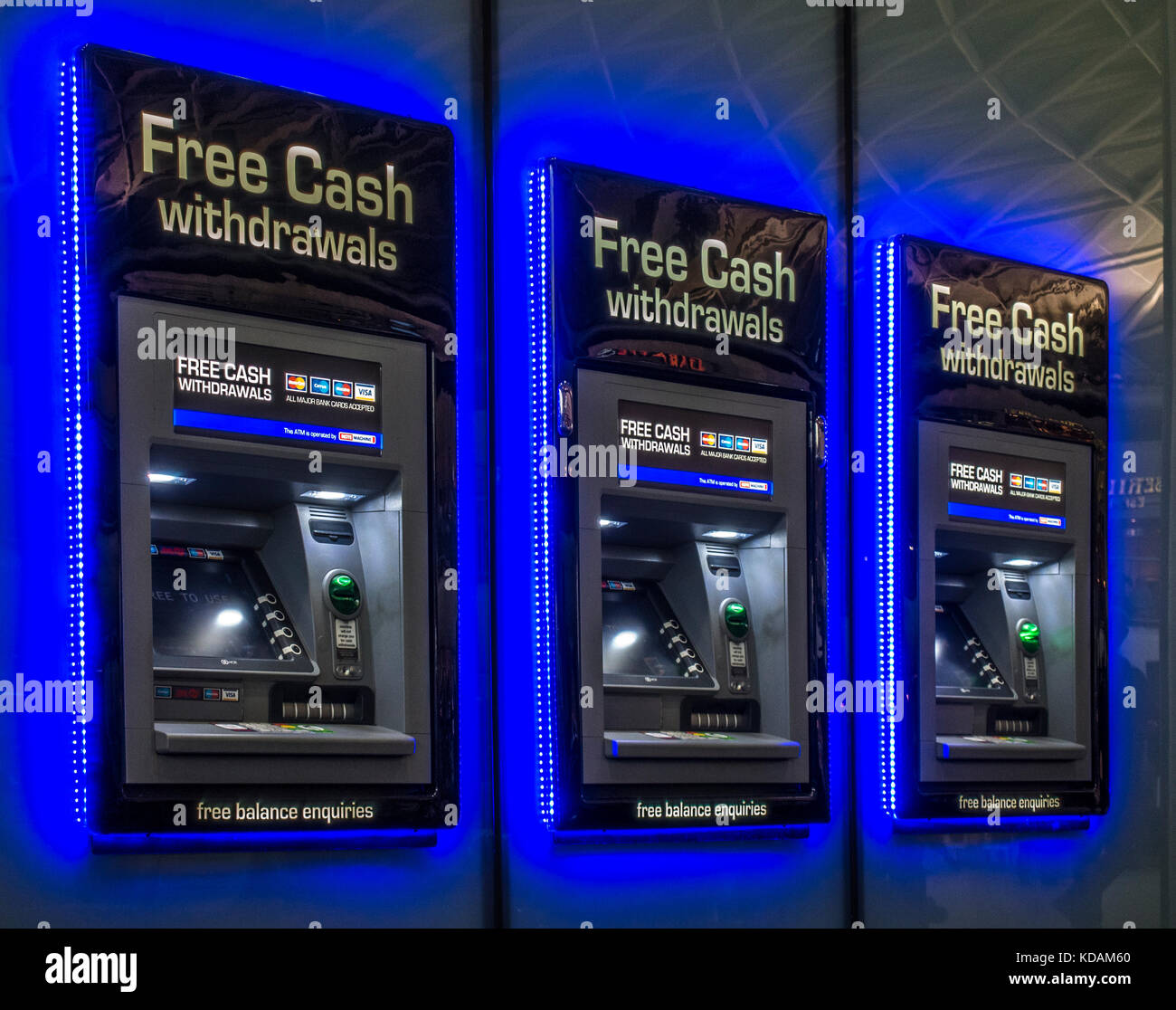 Cash machine / cashpoint / ATM facility, with a row of three machines with bright glowing blue lighting, at Kings Cross Station, London, England, UK. Stock Photo