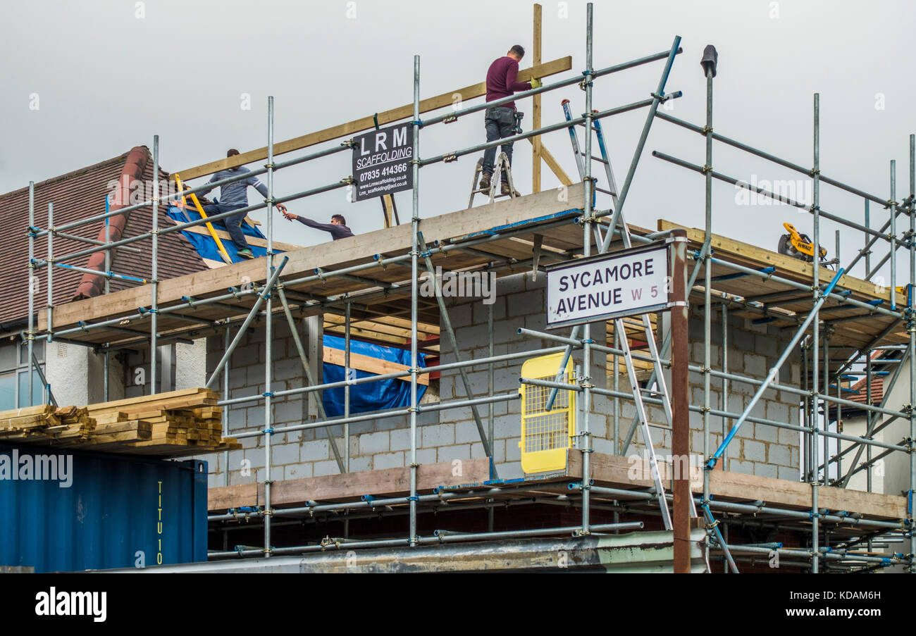 Builders, surrounded by scaffolding, working on the upper floor of a two storey corner house extension, in South Ealing, West London W5, England, UK. Stock Photo