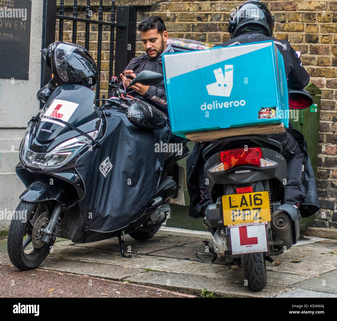 Two male deliveroo (online food delivery company) motorbike riders, taking a break from delivering orders in London, England, UK. Stock Photo