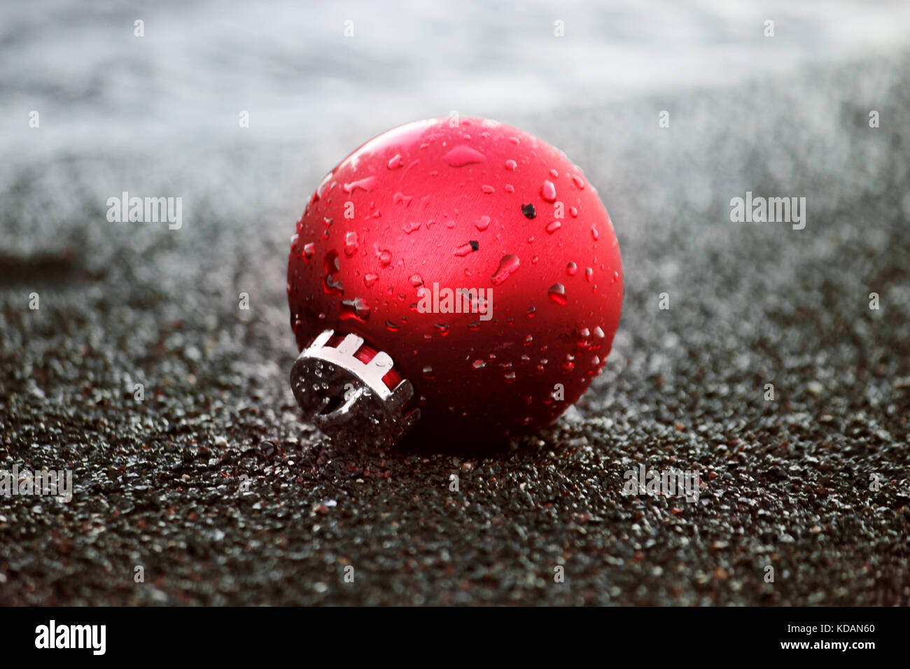 Red Christmas ornament with water drops on the black sand Stock Photo