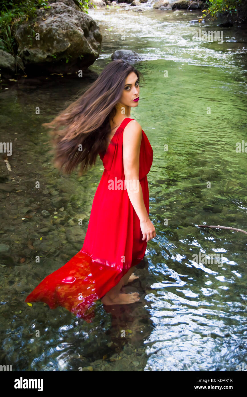 Beautiful woman on the bank of a mountain river with an evening dress ...