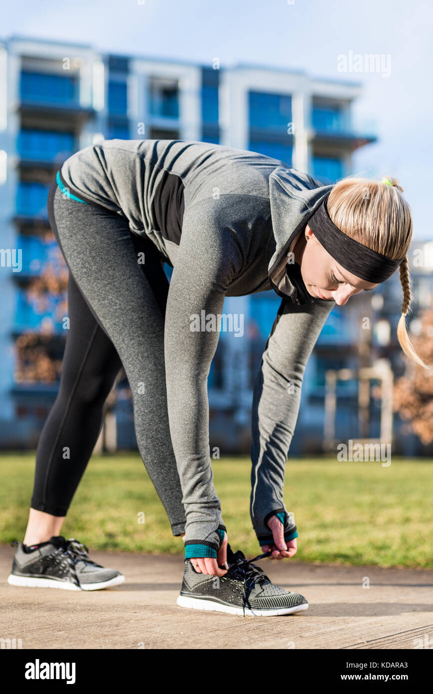 Young woman tying the shoelaces of her shoes while wearing trend Stock Photo