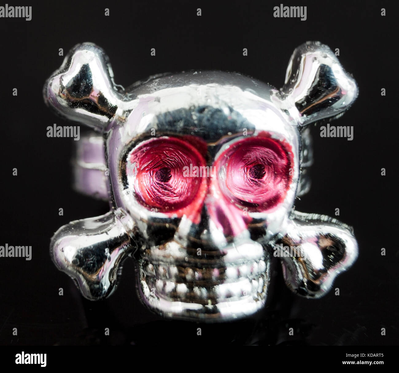 Close up of toy plastic silver skull and crossbones ring on black background. Stock Photo