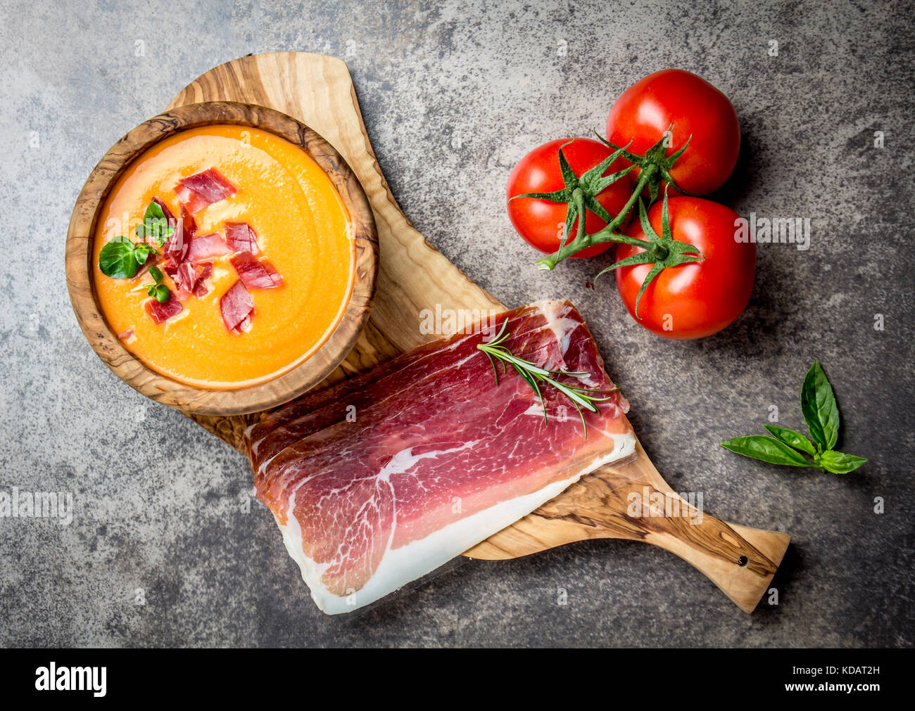 Spanish tomato soup Salmorejo served in olive wooden bowl with ham jamon serrano on stone background. Top view. Stock Photo