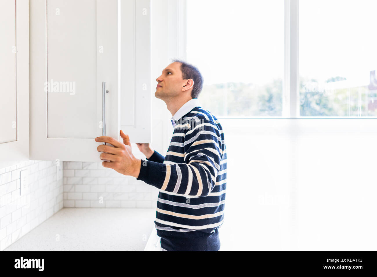 Young man checking looking inside empty kitchen modern cabinets by window after or before moving in Stock Photo
