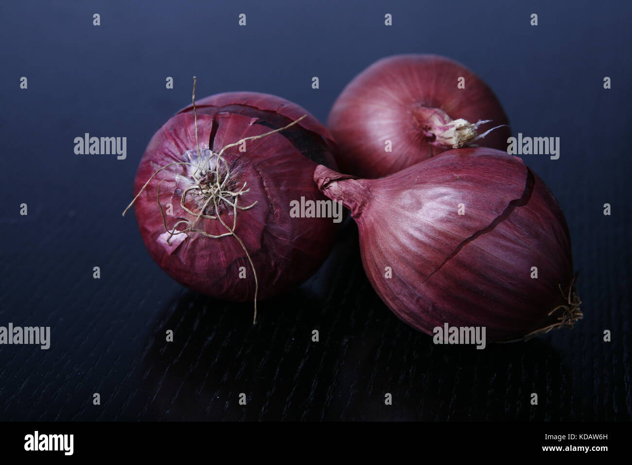 drei Rote Zwiebeln auf schwarzem Tisch - three red onions on black table Stock Photo