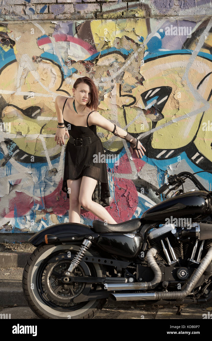 Pretty girl in a short black dress and high heels with a motorcycle