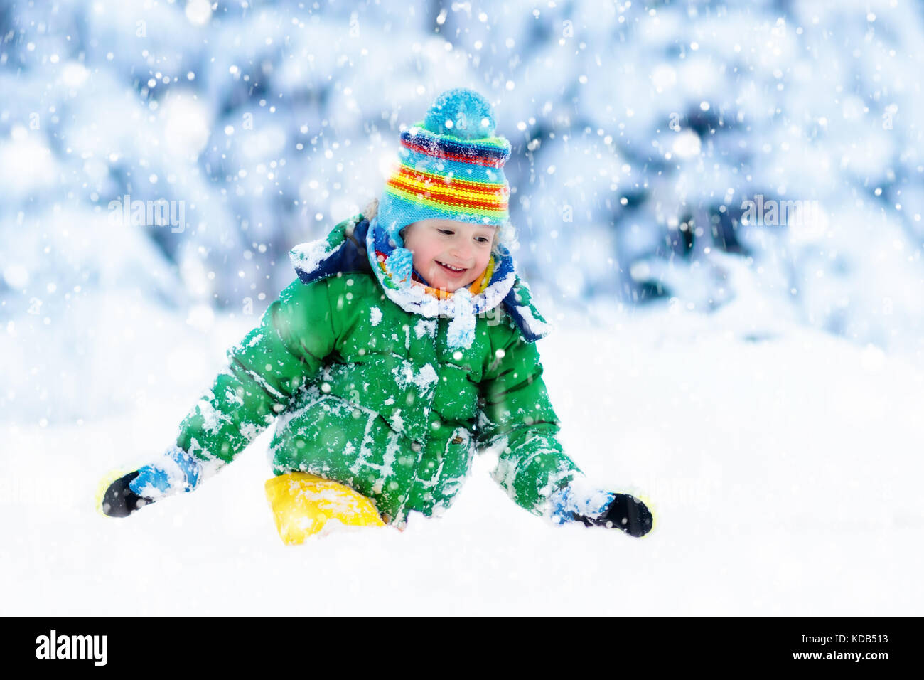 Child playing with snow in winter. Little boy in colorful jacket and ...