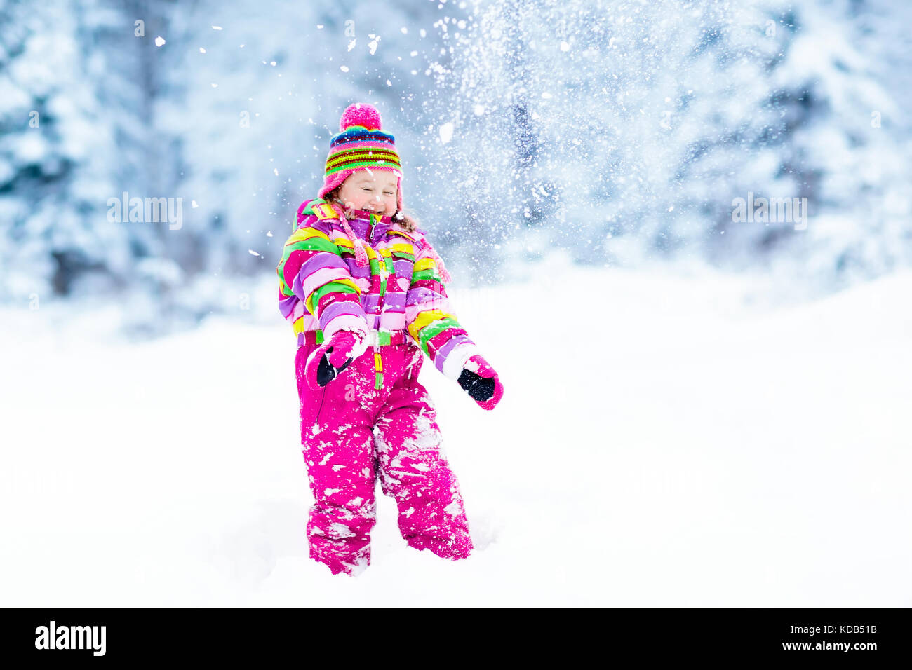 Child playing with snow in winter. Little girl in colorful jacket and ...